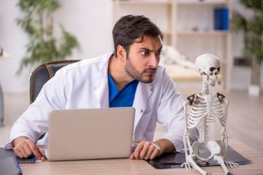 Genç erkek doktor klinikte insan iskeleti üzerinde çalışıyor.