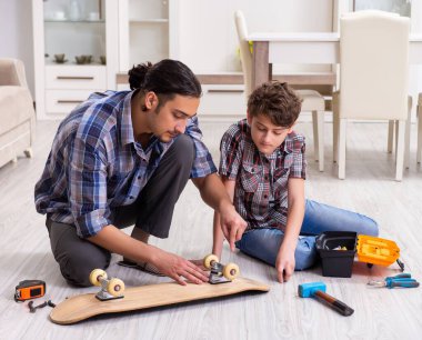 Genç baba oğluyla birlikte kaykay tamir ediyor.