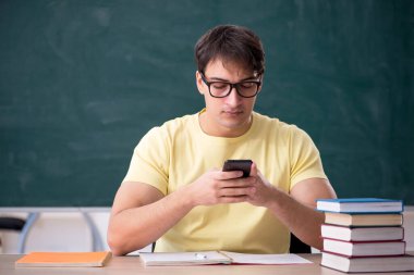 Genç öğrenci yeşil panonun önünde oturuyor.