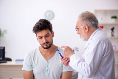 Genç hasta yaşlı erkek doktoru ziyaret ediyor.