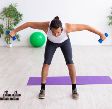 Genç yakışıklı adam içeride spor egzersizleri yapıyor.
