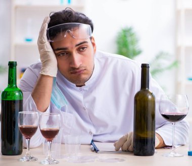 Erkek kimyager laboratuvarda şarap örneklerini inceliyor.