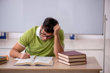 Sınıfta beyaz tahtanın önünde oturan genç öğrenci.