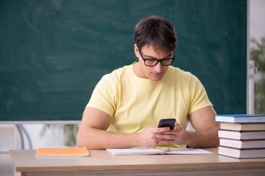 Genç öğrenci yeşil panonun önünde oturuyor.