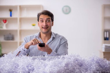 Genç bir işadamı ve işyerinde kesilmiş bir sürü kağıt.