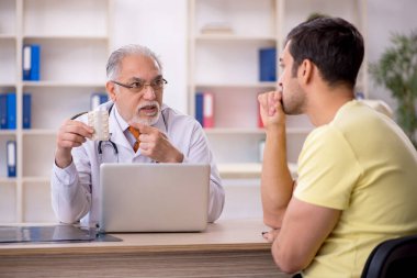 Genç hasta yaşlı doktoru ziyaret ediyor.