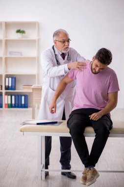 Genç hasta yaşlı erkek doktoru ziyaret ediyor.