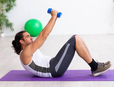 Genç yakışıklı adam içeride spor egzersizleri yapıyor.