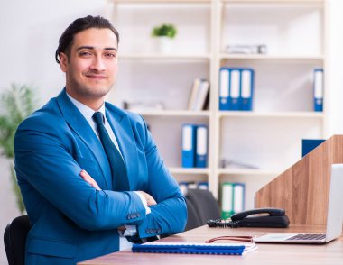 Genç yakışıklı işadamı ofiste oturuyor.