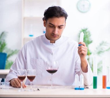 Erkek kimyager laboratuvarda şarap örneklerini inceliyor.