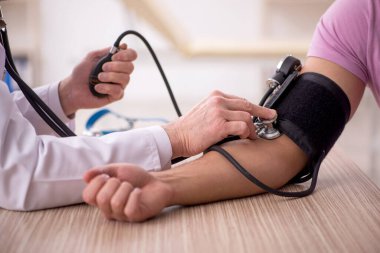 Genç hastaların tansiyonunu ölçen yaşlı bir doktor.