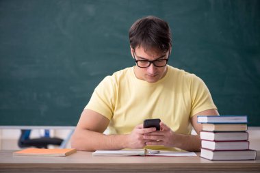 Genç öğrenci yeşil panonun önünde oturuyor.