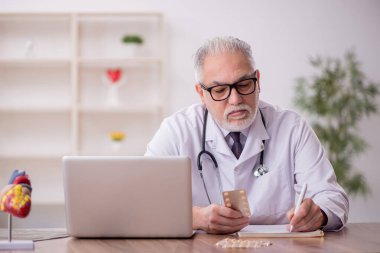 Yaşlı erkek doktor klinikte hap öneriyor.