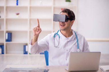 Genç erkek doktor klinikte sanal gözlüklerin keyfini çıkarıyor.