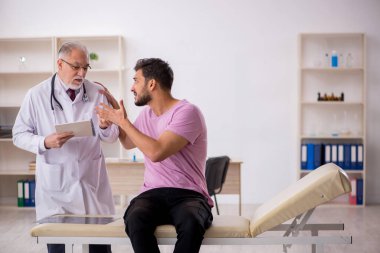 Genç hasta yaşlı erkek doktoru ziyaret ediyor.