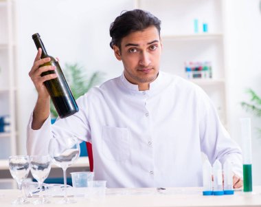 Erkek kimyager laboratuvarda şarap örneklerini inceliyor.