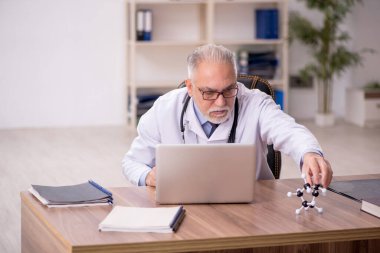 Yaşlı doktor klinikte moleküler model üzerinde çalışıyor.