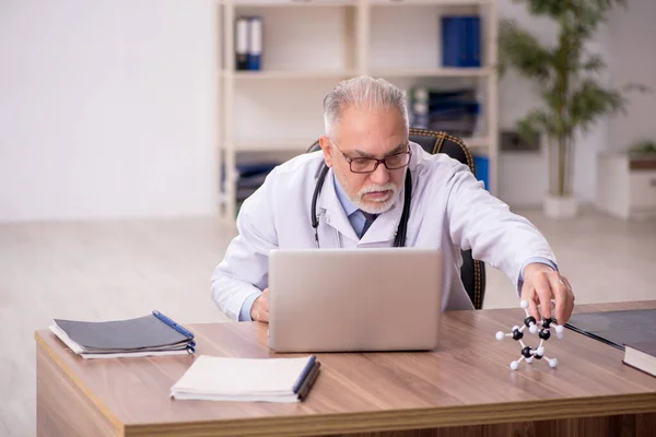 Old doctor studying molecular model in the clinic