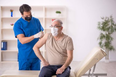 Yaşlı hasta aşılama konseptinde genç erkek doktoru ziyaret ediyor.