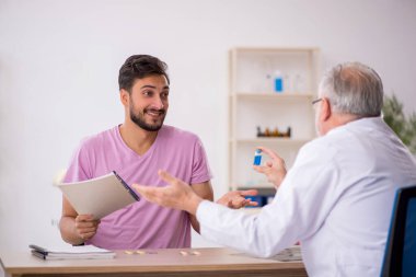 Genç hasta yaşlı erkek doktoru ziyaret ediyor.