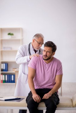 Genç hasta yaşlı erkek doktoru ziyaret ediyor.