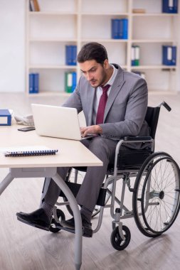 Young male employee in wheel-chair working at workplace