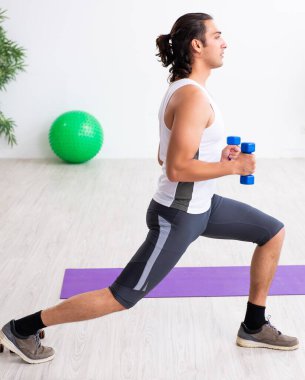 Genç yakışıklı adam içeride spor egzersizleri yapıyor.