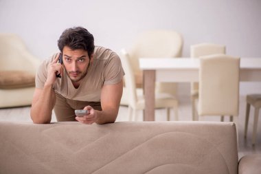 Genç adam salgın sırasında evde televizyon izliyor.