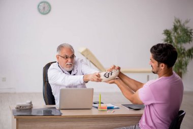 Genç hasta eski erkek doktoru ziyaret ediyor.