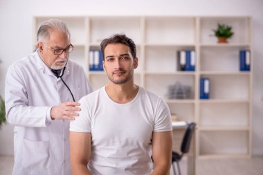 Genç hasta yaşlı erkek doktoru ziyaret ediyor.