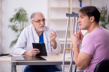 Genç bacağı yaralı hasta yaşlı doktoru ziyaret ediyor.