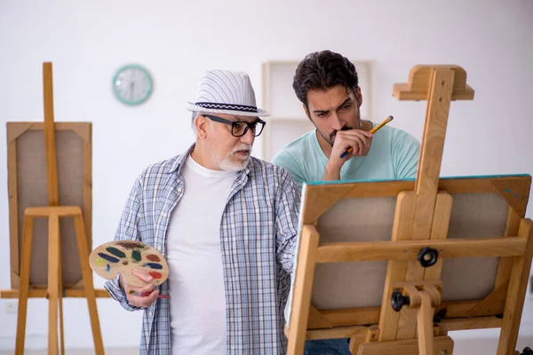 Old male painter teaching young male student at studio