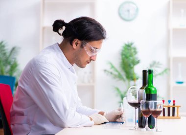 Erkek kimyager laboratuvarda şarap örneklerini inceliyor.