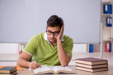 Sınıfta beyaz tahtanın önünde oturan genç öğrenci.