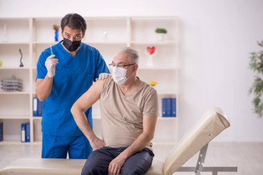 Yaşlı hasta aşılama konseptinde genç erkek doktoru ziyaret ediyor.
