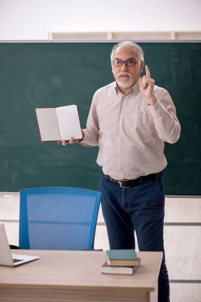 Old teacher in front of green board