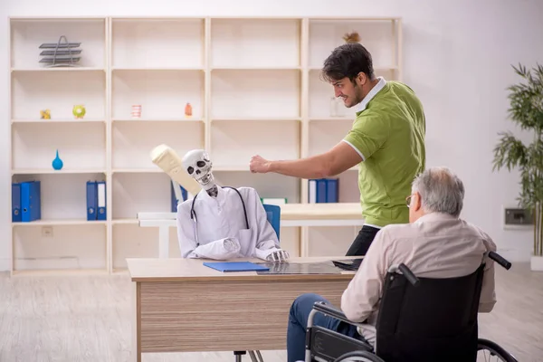 Old male patient in wheel-chair visiting skeleton doctor