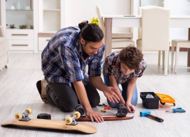 Genç baba oğluyla birlikte kaykay tamir ediyor.