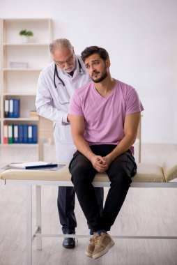 Genç hasta yaşlı erkek doktoru ziyaret ediyor.