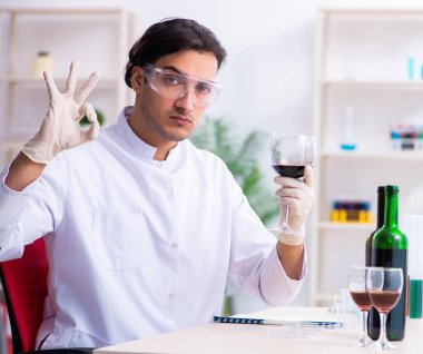 Erkek kimyager laboratuvarda şarap örneklerini inceliyor.