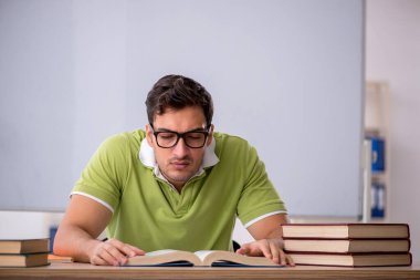 Sınıfta beyaz tahtanın önünde oturan genç öğrenci.