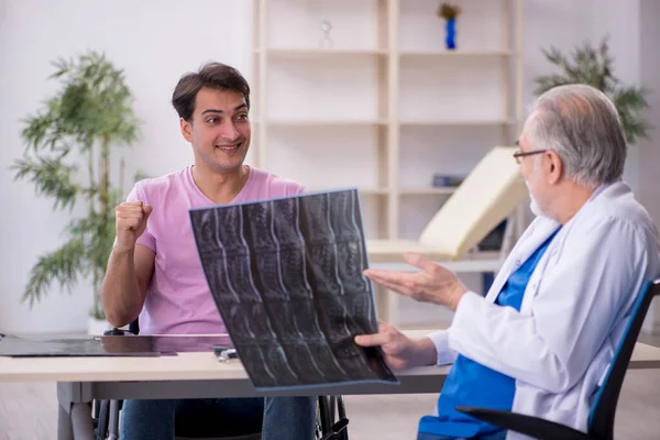 Tekerlekli sandalyedeki genç adam yaşlı doktor radyoloğu ziyaret ediyor.