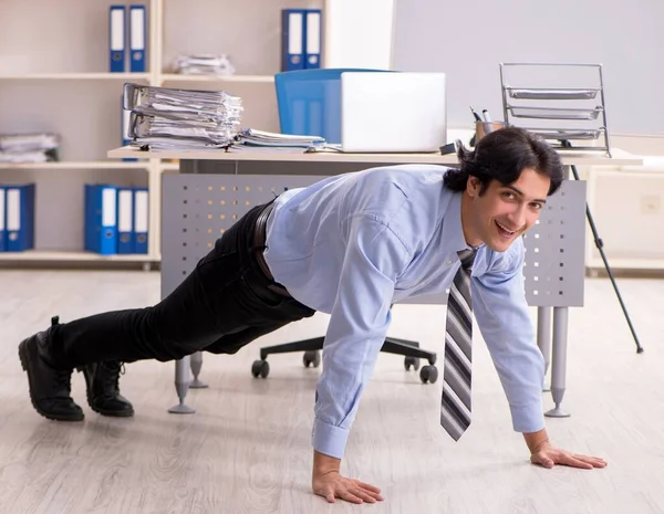 stock image The young handsome male employee doing exercises in the office