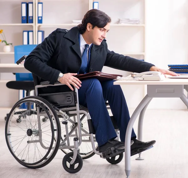 The young male employee in wheelchair working in the office