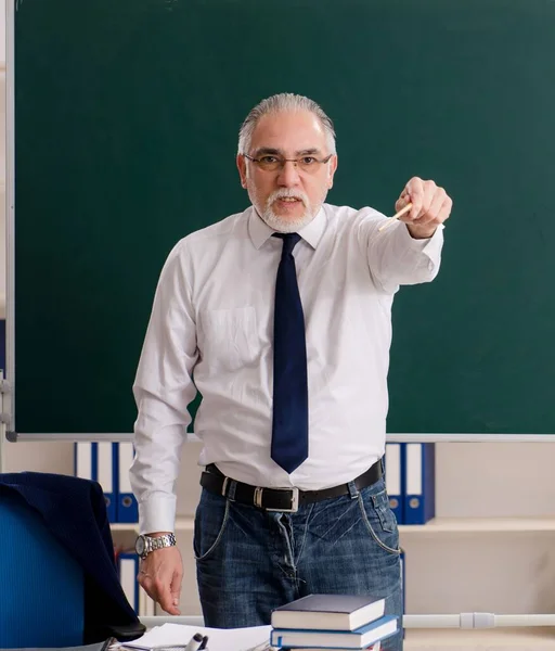 The aged male teacher in front of chalkboard
