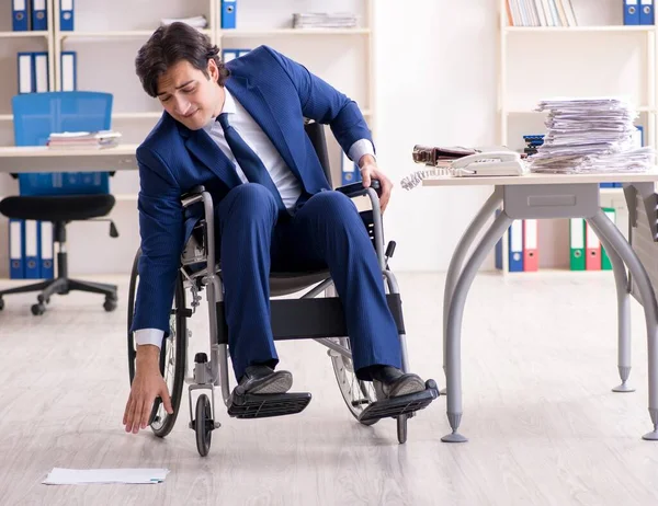 The young male employee in wheelchair working in the office