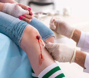 Erkek doktoru ziyaret eden bacağı yaralı genç kadın.