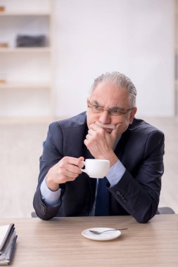 Old employee drinking tea at workplace