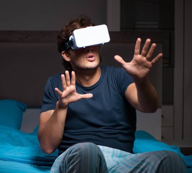 Genç adam gece yatağında bilgisayar oyunları oynuyor.