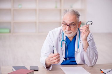 Old doctor holding syringe at the hospital